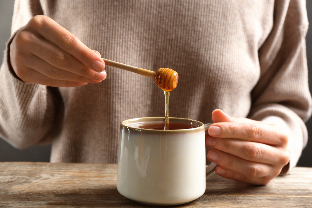 Woman,Putting,Honey,Into,Tea,At,Wooden,Table,,Closeup